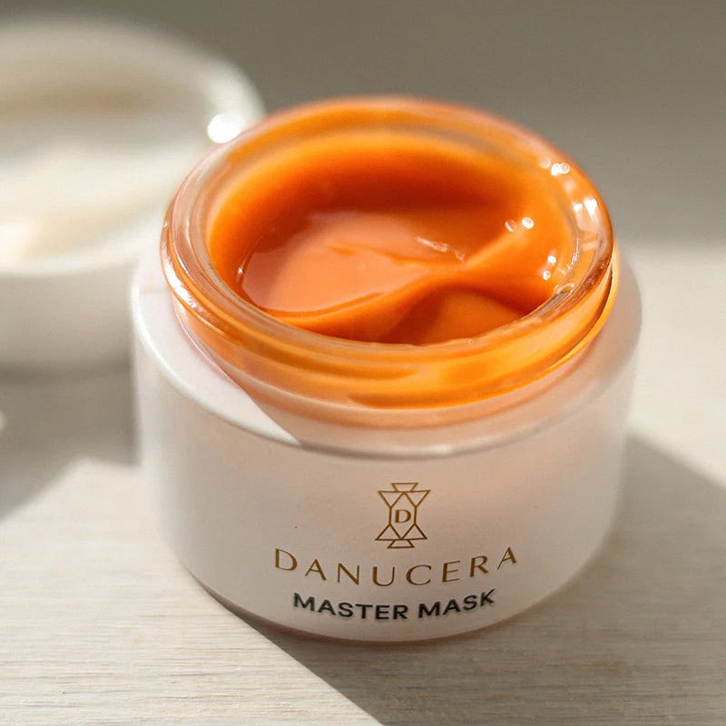 Danucera Master Mask in a white jar with an orange-colored mask visible inside, set on a light wooden surface with a soft-focus background.