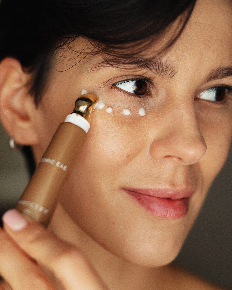 A close-up of a woman applying a eye-cream stick to her under-eye area.