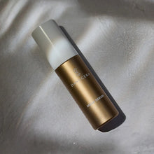 Load image into Gallery viewer, A bottle of Danucera's Magic Serum with a metallic gold body and a frosted white cap, resting on a textured gray surface with soft shadows.
