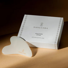 Load image into Gallery viewer, Danucera Sculpting Stone in Afghan White Jade, shown next to its white presentation box on a warm beige surface with dramatic, directional lighting.
